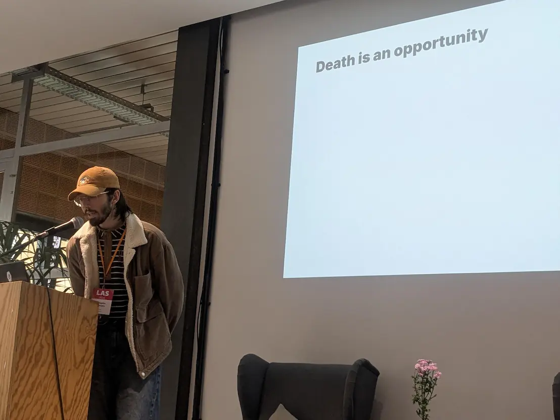 Me on stage speaking on a microphone while there's a projection behind me with the title 'Death is an opportunity'